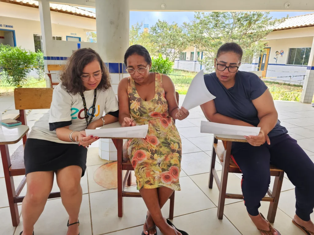 Quatro mulheres em um pátio coberto de uma escola, engajadas em atividades de leitura.