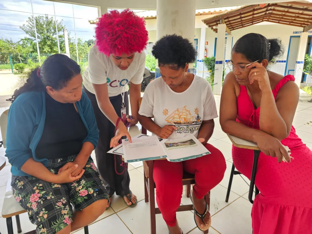 Quatro mulheres em um pátio coberto de uma escola, engajadas em atividades de leitura.