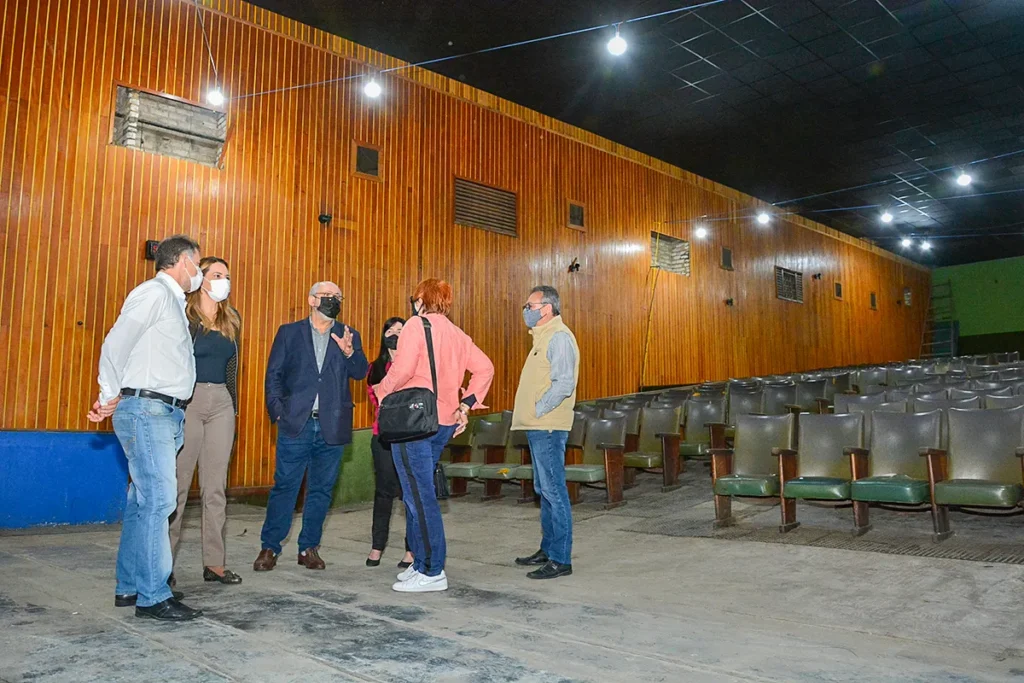 Seis pessoas usam máscaras de proteção facial e conversam em pé no espaço do Cine Madrigal. Uma delas é a prefeita Sheila Lemos.